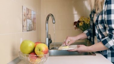 Kadınların elleri mutfak lavabosunda akan suyun altında beyaz bir tabağı süngerle yıkıyor. Evde bulaşık yıkıyorum.