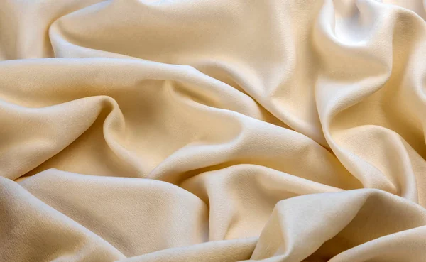 Textile and texture concept - close-up of crumpled fabric background. View from above. Luxury fabric or wavy folds grunge texture, elegant wallpaper design, background, beige fabric