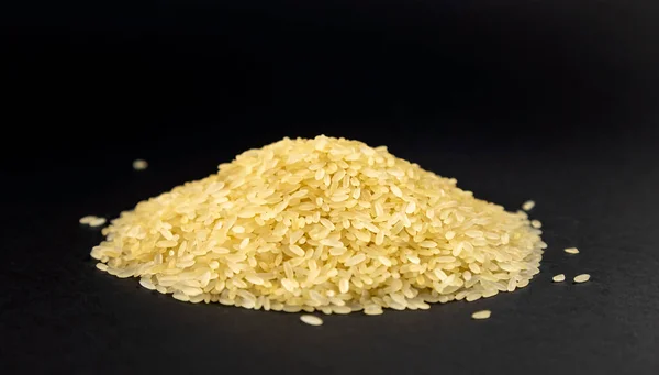A mountain of raw steamed rice grains is piled on a black background. Long rice