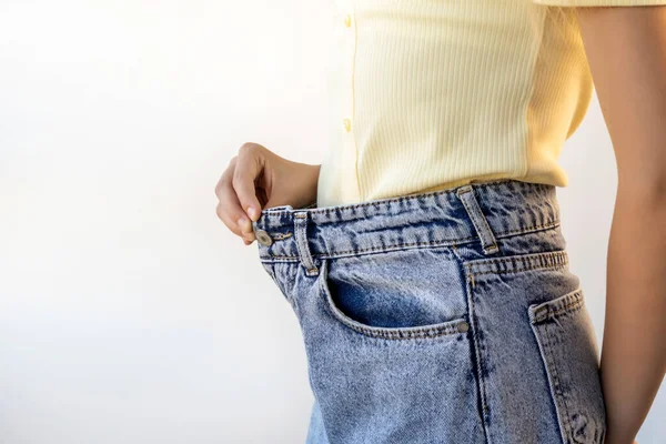 A girl in blue jeans of a large size on a white background. Weight loss and diet