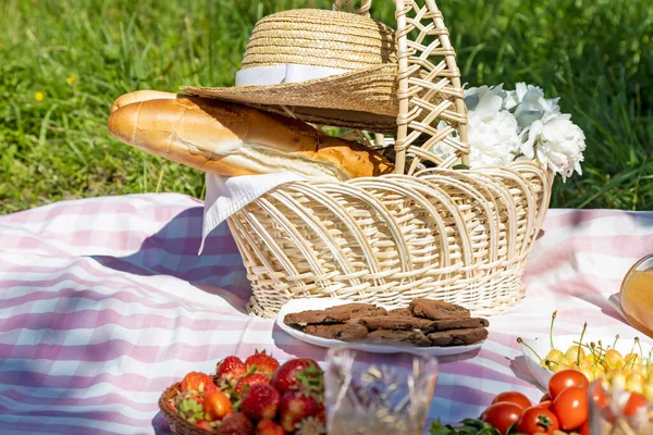 Rest outside the city. French baguette and flowers in a basket covered with a straw hat. Picnic food