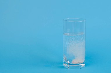 An effervescent tablet that dissolves and fizzes in a glass of water on a blue background. Headache treatment