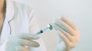 A nurse or doctor in a mask and medical uniform fills a syringe with medicine for injection
