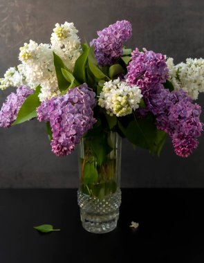 Bouquet of colorful lilac flowers in a glass vase on a dark background