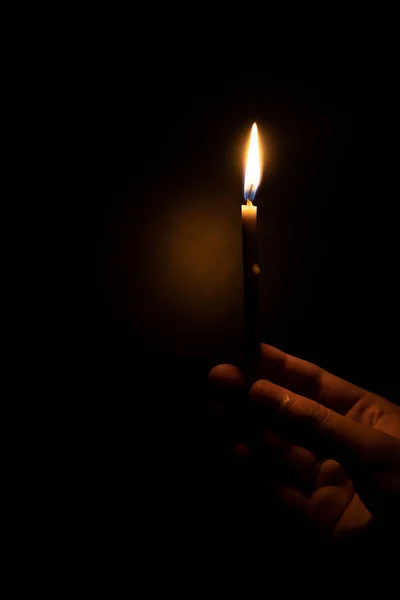 Candle in hand. Female hand holding a burning candle. On a black background
