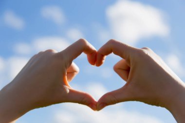 close up of 2 hands create heart shape. Bright blue sky in the background concept of good love valentine positive emotional. Heart in focus