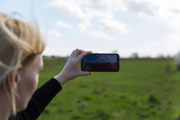 Woman photographs nature scenery on smartphone. Close up of defocused womans face and hands. Phone. Mobility and modern lifestyle concept. Beautiful sky. Young girl taking pictures of the landscape