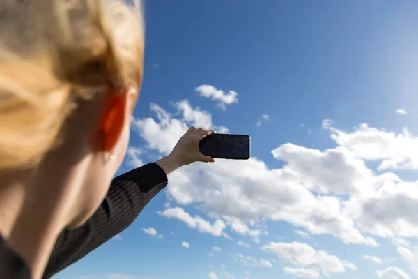 Woman photographs nature scenery on smartphone. Close up of defocused womans face and hands. Phone. Mobility and modern lifestyle concept. Beautiful sky. Young girl taking pictures of the landscape