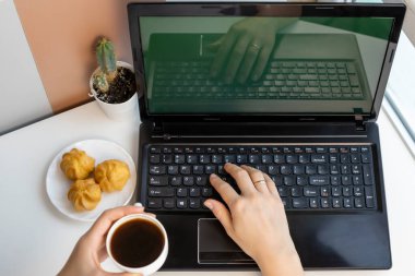 Womans hands holding coffee and delicious cakes. Young woman using laptop while relaxing at home with coffee