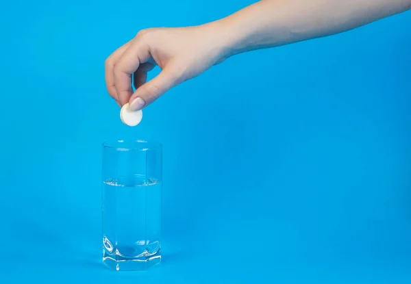 Recovery concept. A womans hand throws an effervescent pill into a glass of water on a blue background. Place for text