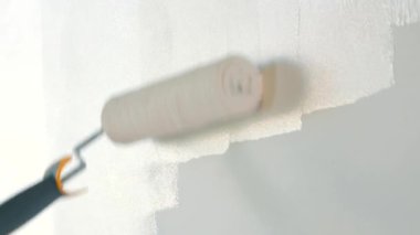 A close-up of the masters hand painting the wall white with a roller