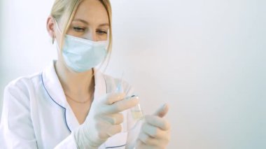 Doktor elinde bir şırınga ve koronavirüs tedavisi aşısı olan bir şişe tutuyor. Bir salgın sırasında iğneler, aşılar ve klinik denemeler