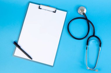 Stethoscope and clipboard with blank white sheet of paper and pen, on blue background. Place for text