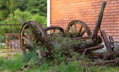 Against the background of a brick house an old broken wooden cart, with broken wheels made of wood.