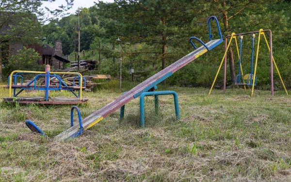 Old swings, abandoned playground equipment, on the background of swings and carousels