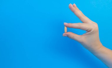 Female hand holding a white pill on a blue background with copy space. The concept of treatment, pharmacy, healthcare.