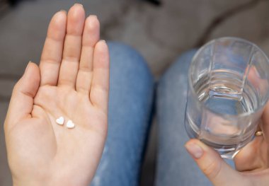 Woman holding pills and glass of water, medicine and medical recovery. Photo of a woman who takes medicine every day. Healthcare concept