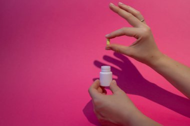 Bir doktor acil tıbbi bakım için beyaz kavanozdan bir hap çıkarır. Pembe arka planda bir elin gölgesi.