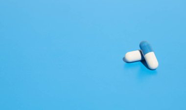 İlaç sanayisi. Mavi arka planda izole edilmiş iki hapı kapat. Ağrı kesici ve ilaç. Beyaz-mavi kapsüller