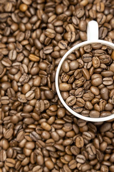 Vertical photo of a cup of coffee full of coffee beans. Top view of white cup and roasted coffee beans