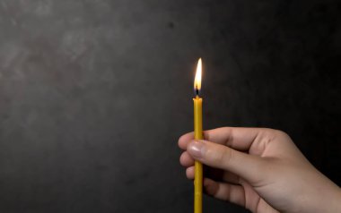 Candle in hand. Female hand holding a burning candle. On a black background