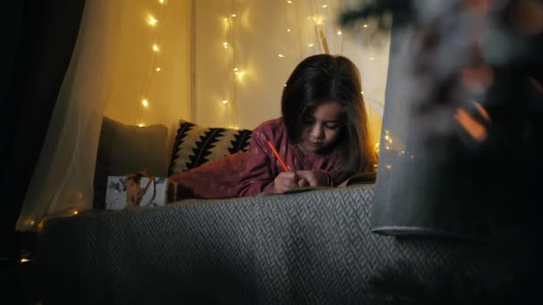 Nettes Mädchen schreibt einen Brief an den Weihnachtsmann mit Wünschen, die auf der Fensterbank liegen, geschmückt mit einer Girlande, Weihnachten — Stockvideo