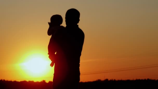 Zorgzame vader houdt de baby in haar armen en kust hem, onherkenbaar silhouet bij zonsondergang — Stockvideo