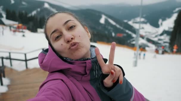 Mulher feliz tira uma foto e selfie contra o pano de fundo de uma estação de esqui — Vídeo de Stock