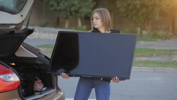 Vrouw grappig proberen om gekochte moderne tv in de kofferbak in de winkel parkeren in close-up — Stockvideo