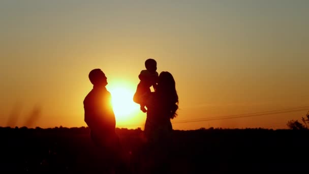 Ouders kussen en knuffelen hun baby, onherkenbaar silhouet van een gezin bij zonsondergang, familiewaarden — Stockvideo