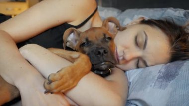 Güzel, genç bir kadın köpeğiyle birlikte evde uyuyor. Yakından sevimli bir köpek yavrusuna sarılıyor.