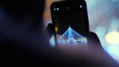 Şehrin önde gelen Noel ağacının cep telefonuyla fotoğrafını çeken bir kadın.
