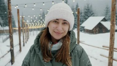 Kış ormanlarında kar yağarken kameraya bakan mutlu güzel bir kadının portresi.