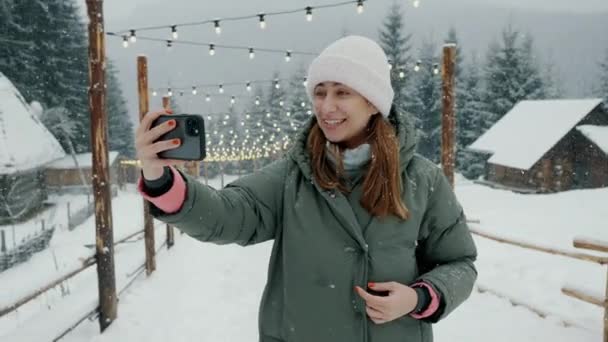 눈덮인 숲 속에서 휴대 전화로 비디오 통화를 하는 행복 한 여성 관광객, 산에 셀카를 타는 여성. — 비디오