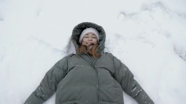 Ovanifrån: lekfull ung kvinna gör en snöängel på snön och kastar en snöboll. — Stockvideo