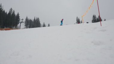 Snowboardcu yavaş çekimde bir kayak merkezinde yokuş aşağı gidiyor, kış dağlarında dinleniyor..