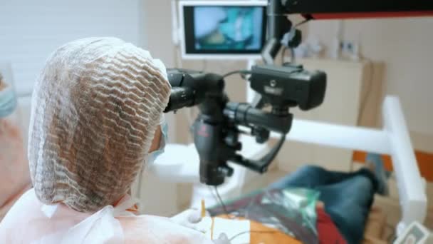 Vrouwelijke tandarts op zoek door een tandheelkundige microscoop tijdens de behandeling van een patiënt tanden — Stockvideo