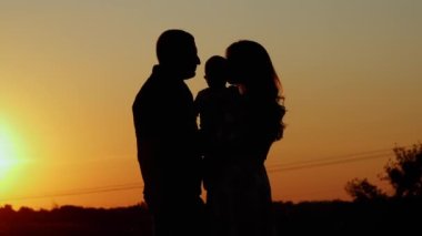 Gün batımında tanınmaz hale gelen aile silueti, aileler çocuklarına sarılıp öperler, aile değerleri ve ebeveyn sevgisi..
