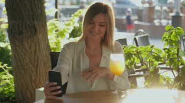 Kadın, arkadaşlarıyla kafede video bağlantısı yoluyla konuşuyor ve soğuk yaz kokteyli içiyor.