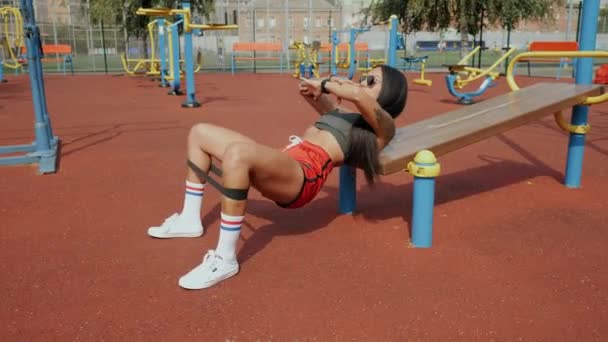 Sportif güzel bir kadın spor sahasında spor salonunda spor lastiğiyle kalça köprüsü yapıyor. — Stok video