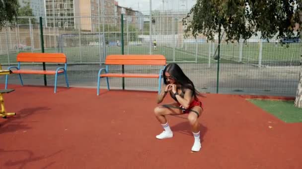 Mulher atlética se agachando, fortalecendo as pernas com uma banda de fitness no chão de esportes no verão — Vídeo de Stock