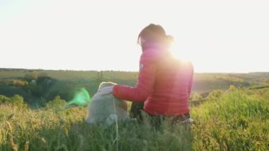 Kadın gün batımında köpeğine sarılıyor. Pug ve kadın doğada oturur ve tepelerde dinlenir, uzaklığa bakarlar.