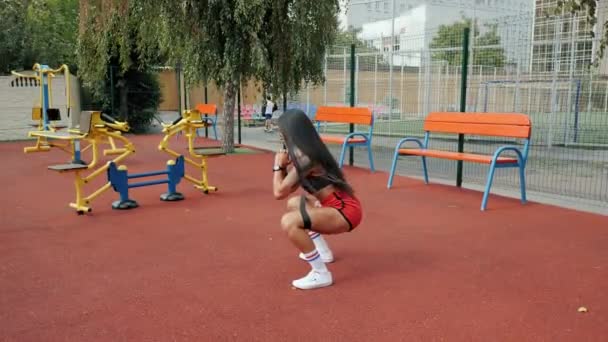 Mulher atlética se agachando, fortalecendo as pernas com uma banda de fitness no chão de esportes no verão — Vídeo de Stock