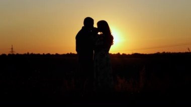Ebeveynler bebeklerini öper ve kucaklarlar. Gün batımında tanınmaz bir aile silueti. Aile değerleri.