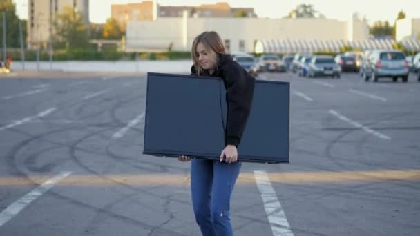 Woman funny trying to put purchased modern tv in car trunk at store parking in close-up — Stock Video