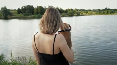 Göl kenarındaki şirin, küçük Alman boksör yavrusunun portresi. Kadın kollarına köpek alıp sarılıyor. 