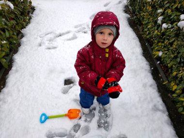 Kışlık botları olmadan karda oynayan çocuk.