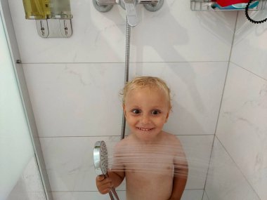 Çocuk duşta yıkanır ve surat yapar.