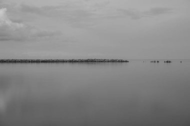 Kıyısı ve gökyüzünde bulutları olan eski bir taş iskele ve sakin sularda bir yansıma.