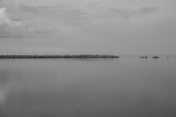 海岸と雲のある古い石造りの桟橋と水の穏やかな広がりの中での反射 — ストック写真
